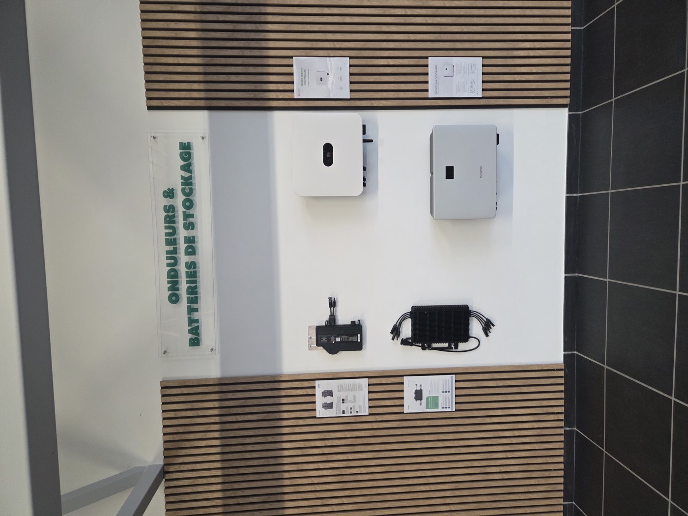 Le mur onduleurs et batteries de stockage du showroom, avec plusieurs modèles accrochés et leurs fiches techniques.