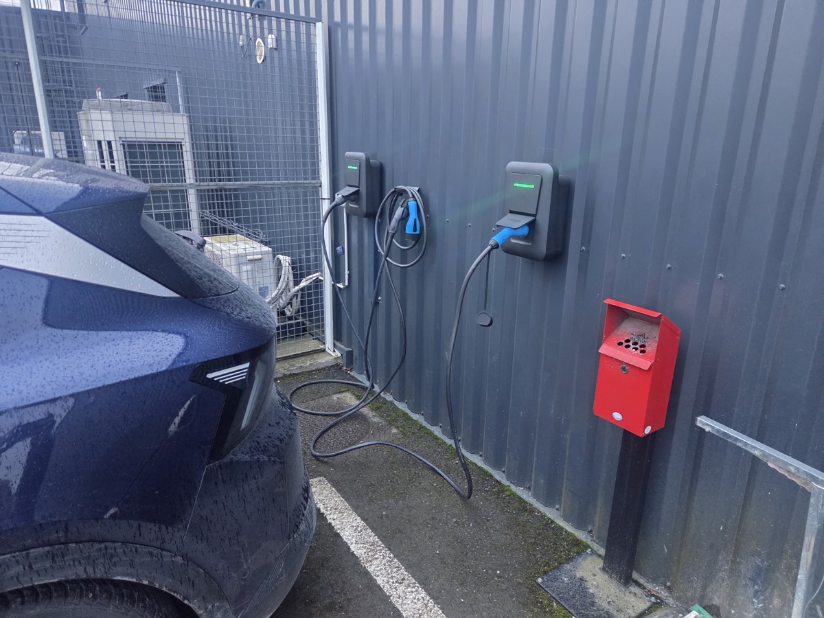 Deux bornes de recharge murales installées sur un bardage, une voiture électrique branchée.