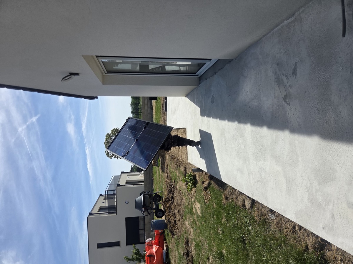 Un installateur porte un panneau photovoltaïque le long de la maison.