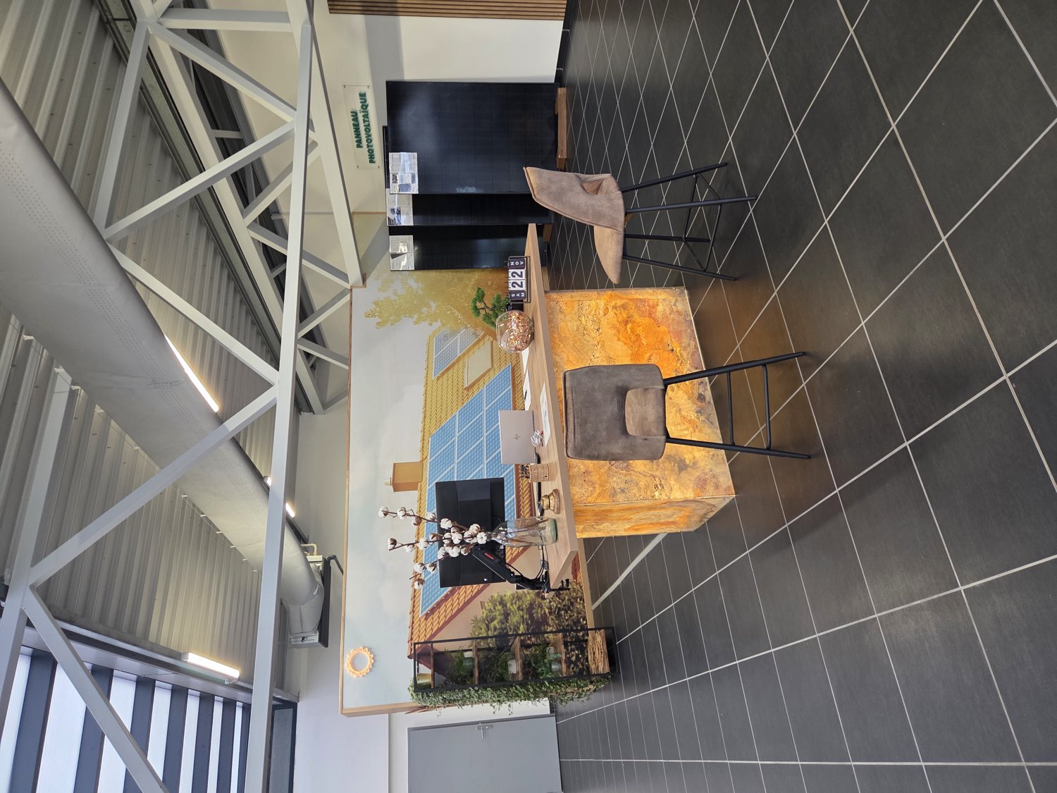 Le comptoir d'accueil en onyx rétroéclairé, devant la fresque peinte d'une maison équipée de panneaux solaires.